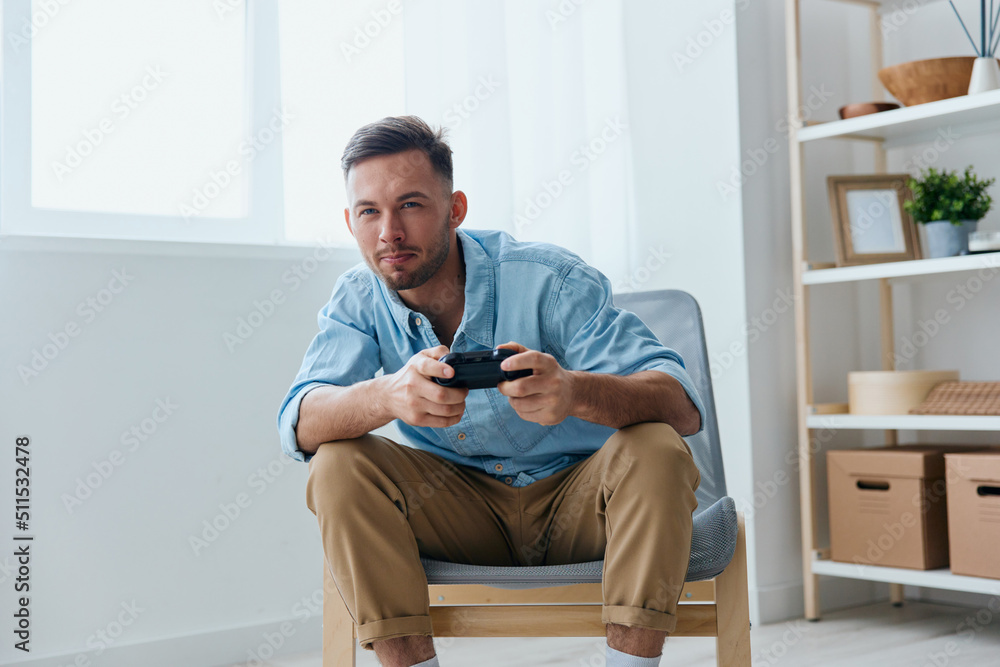 Overjoyed focused young tanned guy hold joystick gamepad looks at screen playing in races at home. Player Stream Platform concept. Relaxing Active recreation. Copy space for game console advertising Overjoyed focused young tanned guy hold joystick gamepad looks at screen playing in races at home. Player Stream Platform concept. Relaxing Active recreation. Copy space for game console advertising