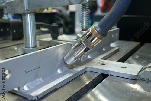 MIG welding torch of a robot working making weld on piece of metal. Production hall photo
