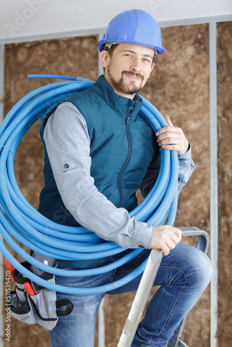 male tradesman with reel of blue pipe on his shoulder