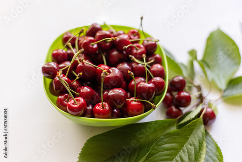 Green plastic bowl filled with cherries on a white background. Cherry fruits on a white background