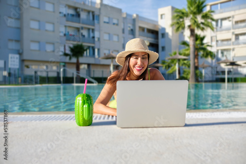 digital nomad woman working remotely online in a swimsuit with long black hair and a laptop in a swimming pool