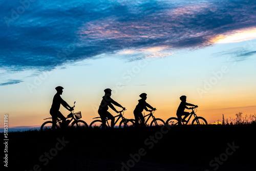 parents and kids ride bicycle at sunset. family on cycle ride in countryside. Silhouette of cyclist