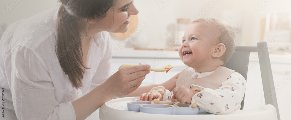 Mother feeding her cute little baby in kitchen. Banner design