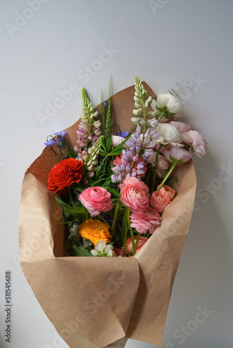 Large colored bouquet of different flowers in kraft packaging on a light background. Gift of expensive fresh flowers