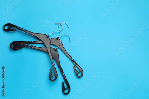 Empty hangers on light blue background, flat lay. Space for text