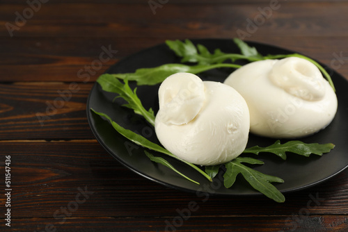 Delicious burrata cheese with arugula on wooden table, closeup