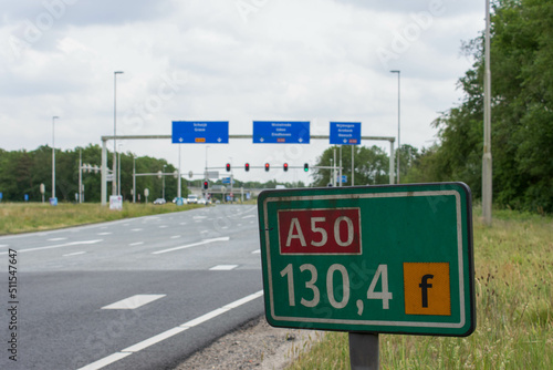 View on junction "Paalgraven" near highway A50. In front a hectometer pole, in the back the junction with a row traffic lights and traffic signs. Oss, North Brabant, the Netherlands - May 26 2022. © PaulvSchijndel