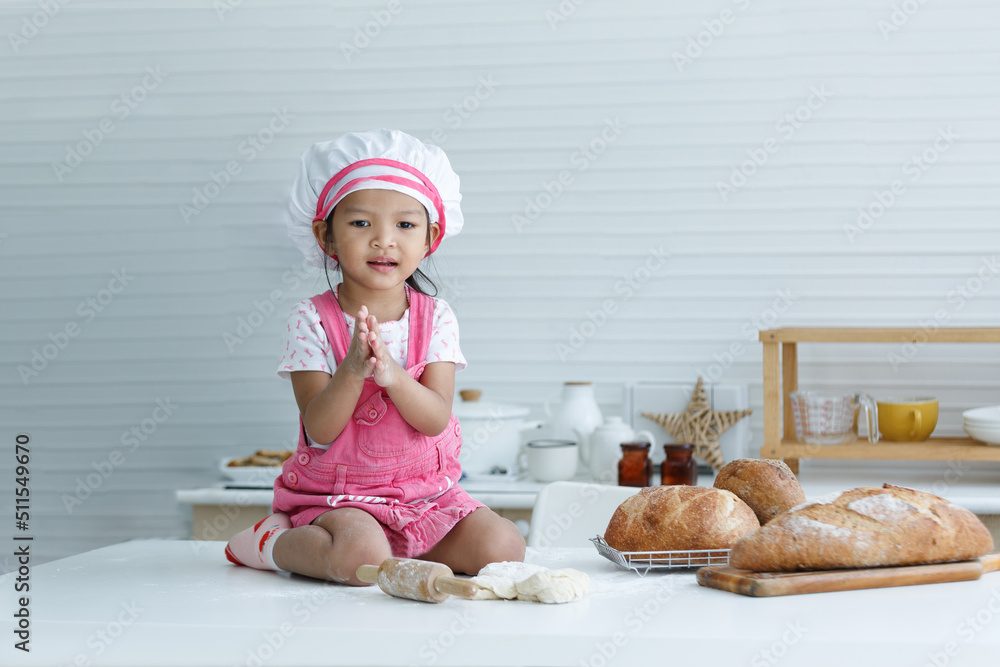 Cute little chef sitting on the table learning to make bread Cute little chef sitting on the table learning to make bread