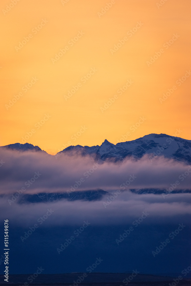 cielo de atardecer anaranjado con montañas azules cubiertas de nubes bajas, contraste de colores, hora dorada atardecer 