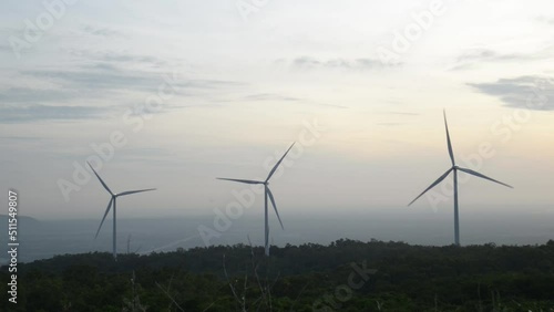 Windmills turn the wind in the middle of mountains, forests and fields.