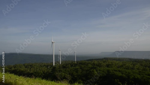 Windmills turn the wind in the middle of mountains, forests and fields.