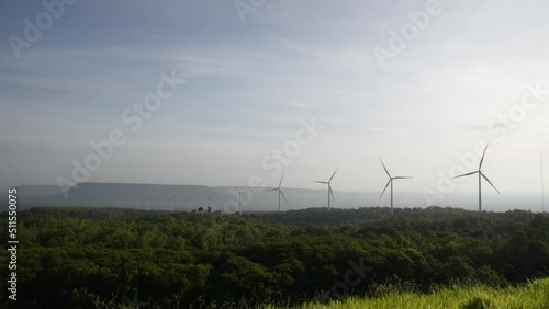Windmills turn the wind in the middle of mountains, forests and fields.
