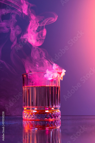 Creative composition with whisky glass and smoke over dark colored background in neon light. Concept of art, taste, decorations, creativity, decor