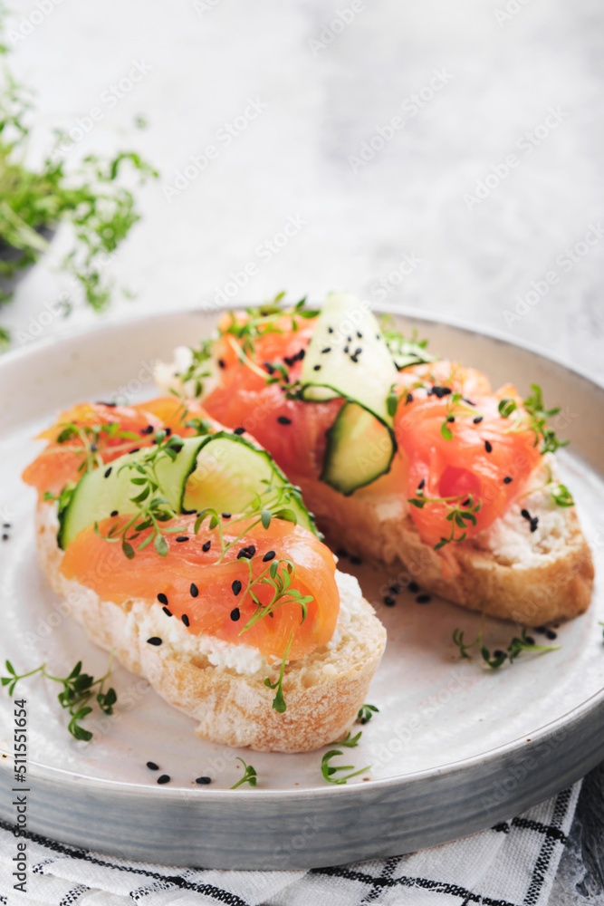 Sandwiches. Salmon toast with cream cheese, cucumber, black sesame and microgreens on gray concrete table background. Seafood. Healthy food. Top view. Sandwiches. Salmon toast with cream cheese, cucumber, black sesame and microgreens on gray concrete table background. Seafood. Healthy food. Top view.