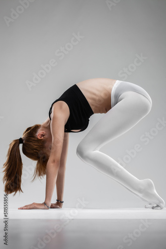Fit ballerina girl stretching and practicing yoga poses against gray background..