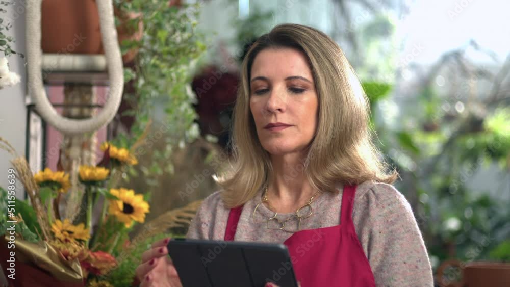 Portrait of Female business owner of flower store holding digital tablet wearing red apron checking online orders Portrait of Female business owner of flower store holding digital tablet wearing red apron checking online orders