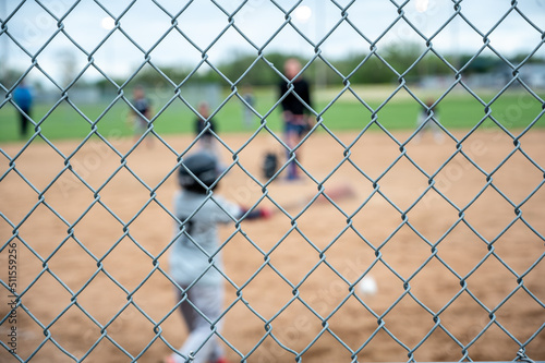 Konstfotografi Selective focus on chain link fence with a youth baseball game defocused and blu