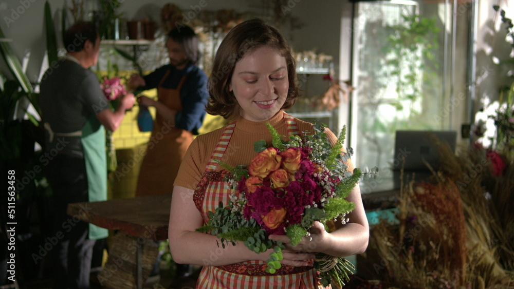Female Florist inside flower shop holding bouquet. Portrait of young employee smiling