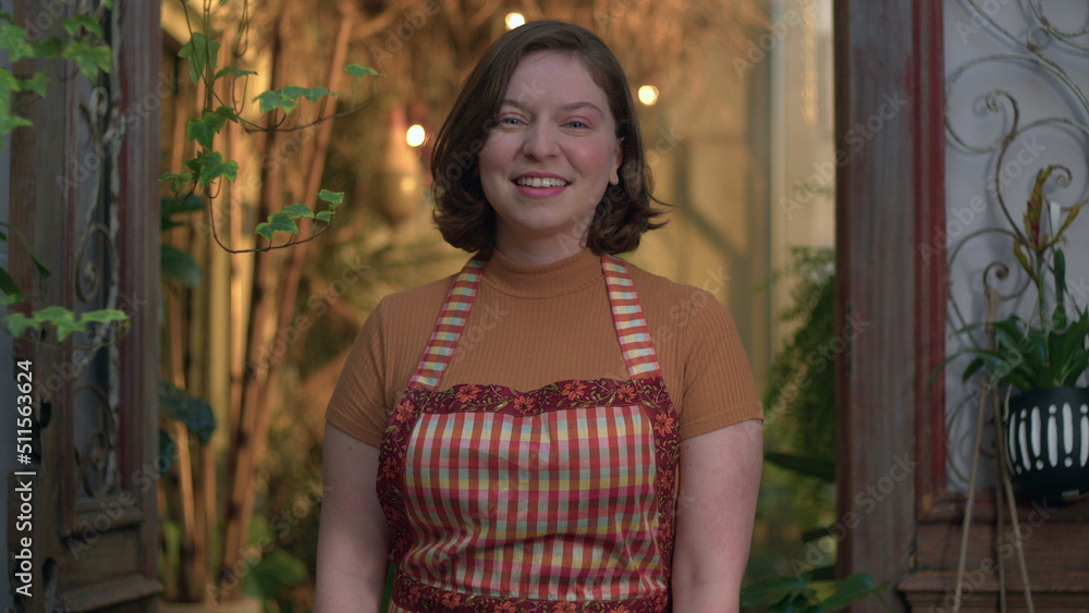 Naklejka premium Small business store female employee portrait standing inside local shop smiling at camera wearing apron