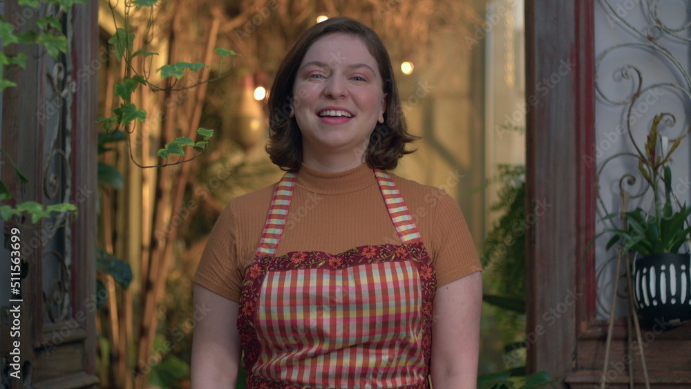 Naklejka premium Portrait of young woman employee at small business flower shop. Female entrepreneur staff wearing apron standing at local store