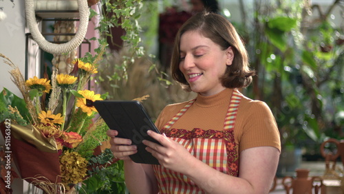 Female employee holding tablet checking inventory at small business flower shop