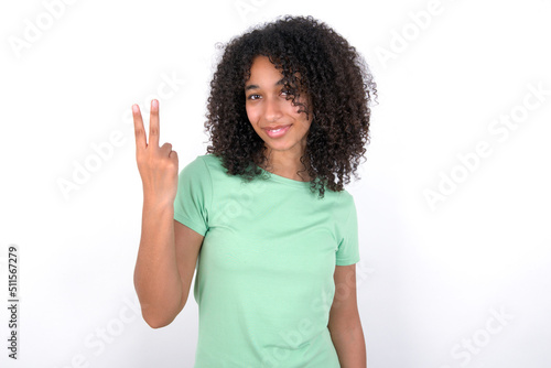 Young beautiful girl with afro hairstyle wearing green t-shirt over white background smiling and looking friendly, showing number two or second with hand forward, counting down
