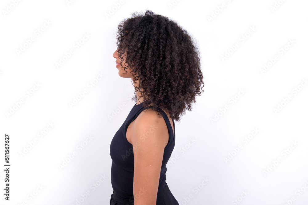 Naklejka premium Young beautiful girl with afro hairstyle wearing black tank top over white background looking to side, relax profile pose with natural face with confident smile.