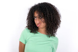 Young beautiful girl with afro hairstyle wearing green t-shirt over white background making grimace and crazy face, screaming out of control, funny lunatic expressing freedom and wild.