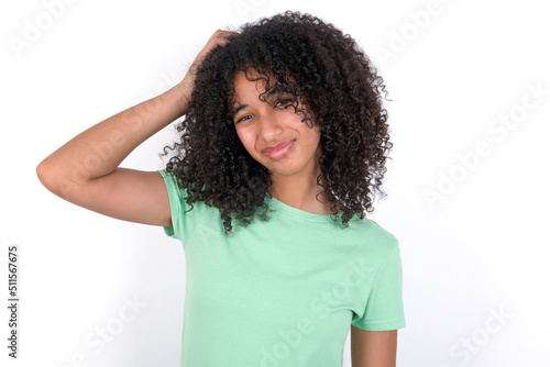 Young beautiful girl with afro hairstyle wearing green t-shirt over white background being confused and wonders about something. Holding hand on head, uncertain with doubt. Pensive concept.