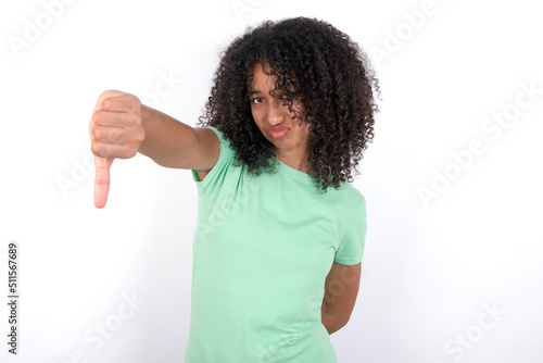 Young beautiful girl with afro hairstyle wearing green t-shirt over white background feeling angry, annoyed, disappointed or displeased, showing thumbs down with a serious look