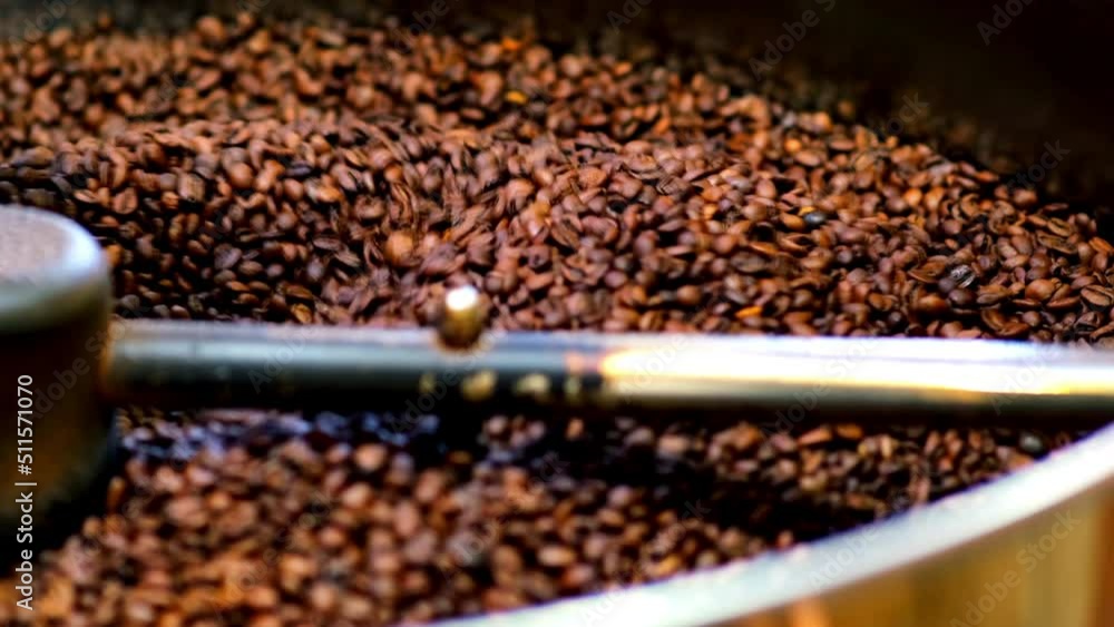 Roasted coffee beans fly and spin on a black background in slow motion. Production of fresh fried coffee beans roasting factory process. Prepared coffee beans mixing around on a cooling plate of oven. Roasted coffee beans fly and spin on a black background in slow motion. Production of fresh fried coffee beans roasting factory process. Prepared coffee beans mixing around on a cooling plate of oven.