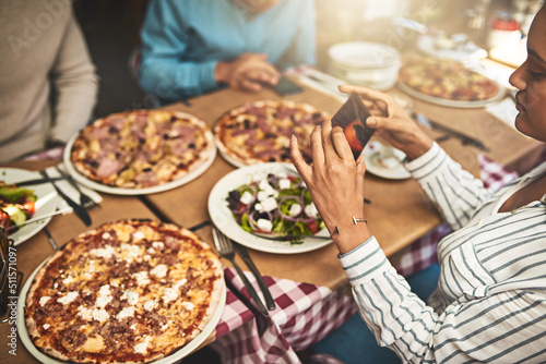 Pizza. Shot of a group of people seated at a table with plates of pizza in front of them while one takes a photo of it inside of a restaurant. photo