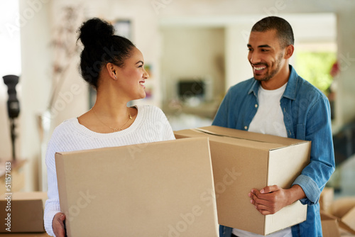 Theyre finally moving in together. Shot of a happy young couple carrying cardboard boxes into their new home.