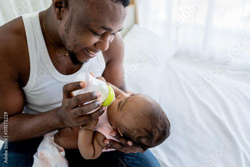 African father Sitting on bed, and feed milk from bottle milk to his 3-month-old baby newborn daughter,  to family and food for baby  newborn concept. photo