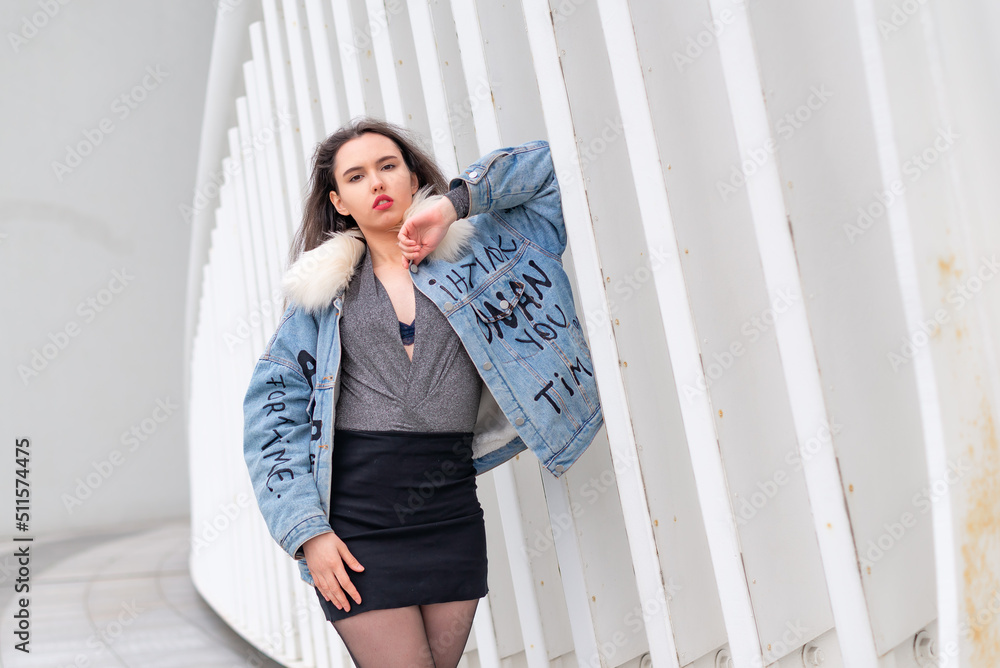 A fashionable girl with a wavy hairstyle and red lips poses on the street. Brunette in a jacket and a black skirt look away to the street .. A fashionable girl with a wavy hairstyle and red lips poses on the street. Brunette in a jacket and a black skirt look away to the street ..