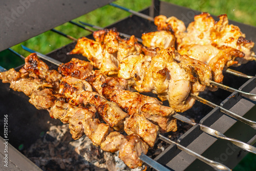 The process of cooking barbecue on a metal grill with burning firewood and smoke.Grilled meat. Cooking for a picnic.Delicious, juicy, aromatic pieces of shashlik.Meadow background.