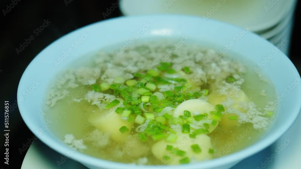 Close up person falling chopped spring onions into bowl of hot Clear Soup with Tofu and Minced Pork, Thai food