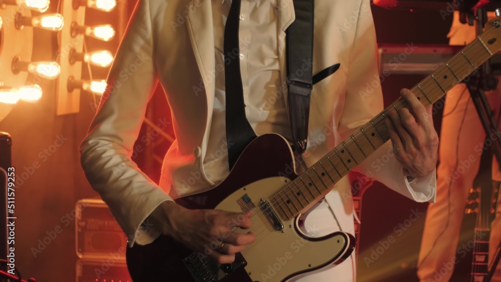Guitarist in a white suit and black tie plays fast solo on a guitar on a stage Guitarist in a white suit and black tie plays fast solo on a guitar on a stage