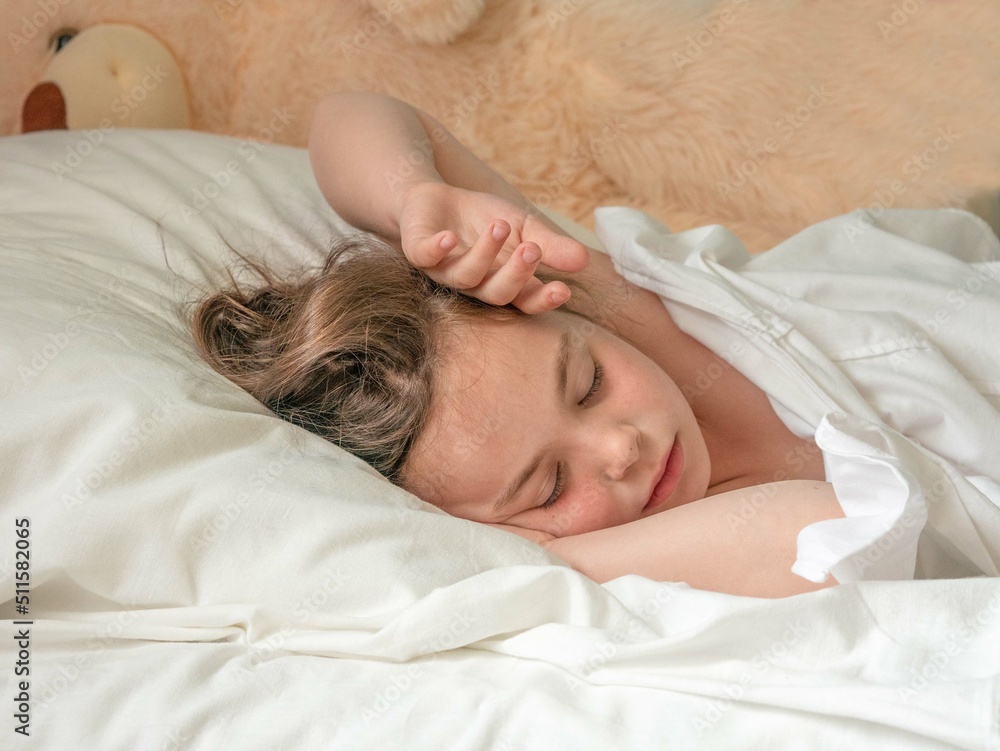 Little curly-haired girl 8 years old sleeps on a white bed Little curly-haired girl 8 years old sleeps on a white bed
