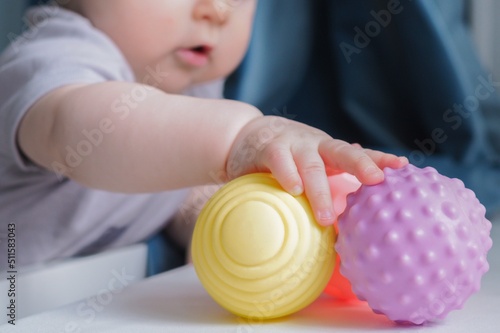 Baby holding a colorful sensory soft ball for babies and kids. Concept of massage textured balls for developing tactile senses.  photo