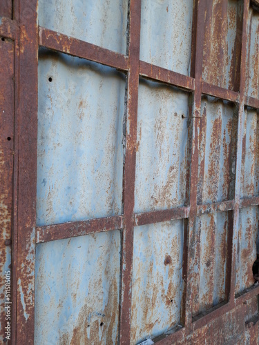 Ventana antigua de metal oxidado en cuadros, con chapas de zinc en la parte de atràs, forma un diseño abstracto en la casa històrica abandonada