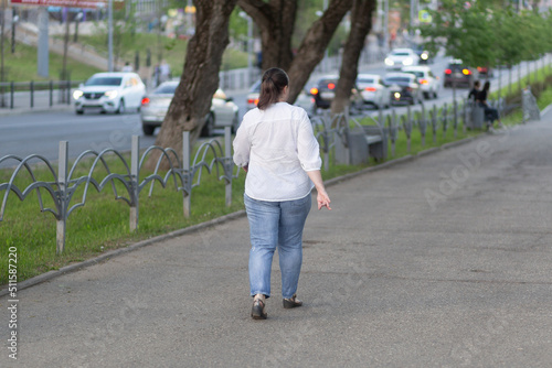 A very fat woman walks down a city street in summer.
