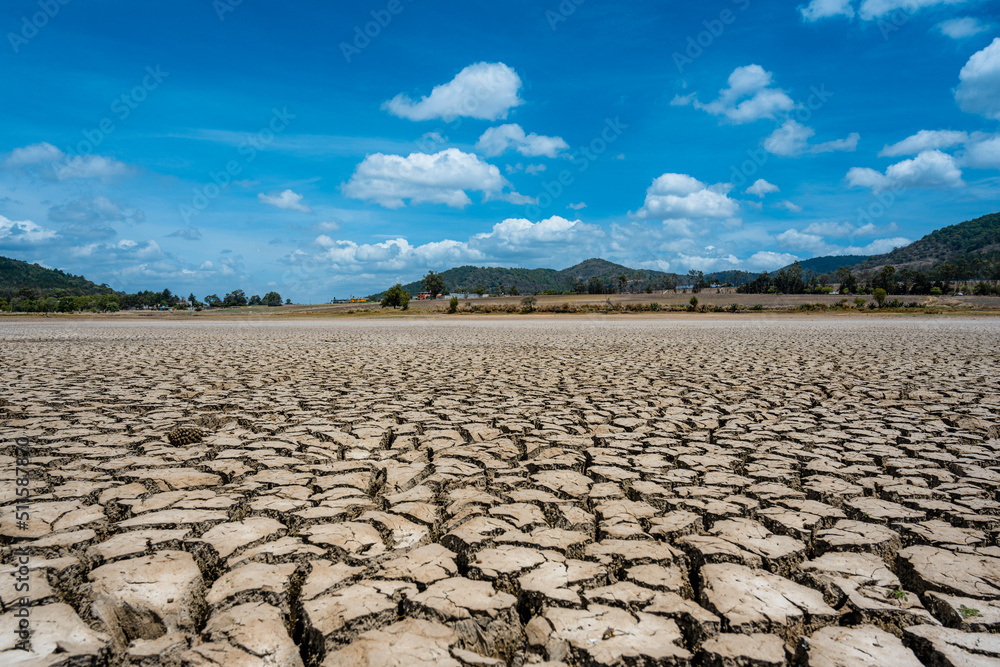 Fototapeta premium Landscape photography of the cracks in the bottom of a dry lake in the background of a house and the blue sky at noon