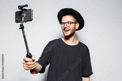 Happiness guy making video by smartphone with selfie stick on grey background.