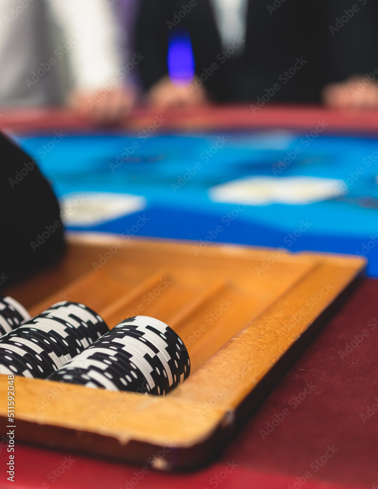 Fototapeta premium Poker table view with a pack of cards, tokens, alcohol drinks, dollar money and group of gambling rich wealthy people playing poker in casino, with croupier