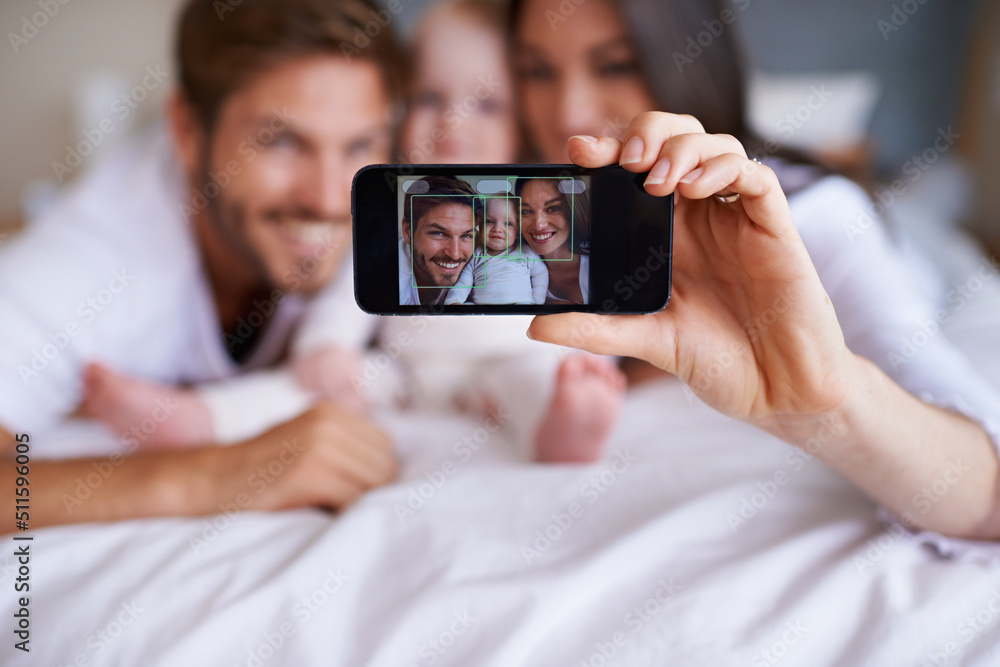 Smile for the family selfie. Shot of a young couple lying on the bed with their baby girl and taking a selfie with their mobile phone.