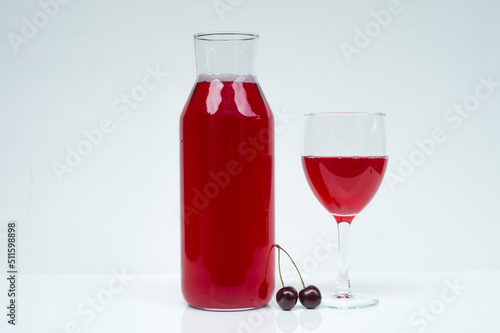 homemade cherry drink isolated on white background.bright red cherry drink in a bottle and a glass with a natural cherry in the middle on a white background with empty space for text