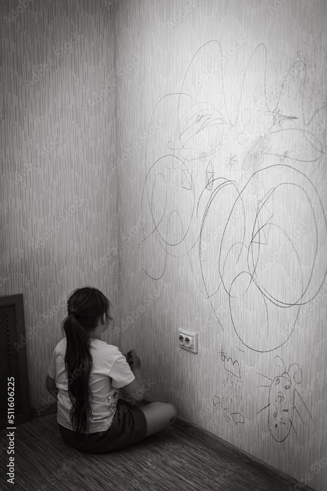 Naklejka premium Back view of little naughty girl with dark hair wearing T-shirt, holding green marker in hand, sitting on floor, drawing picture of bug on old yellow wallpaper. Misbehavior, redecoration. Vertical.