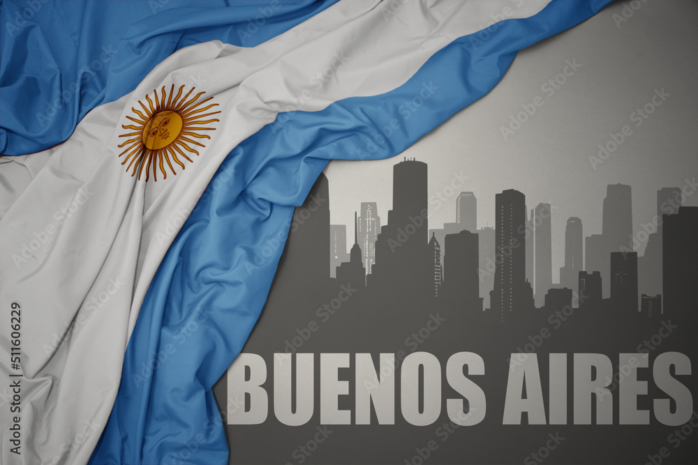 abstract silhouette of the city with text Buenos Aires near waving national flag of argentina on a gray background.