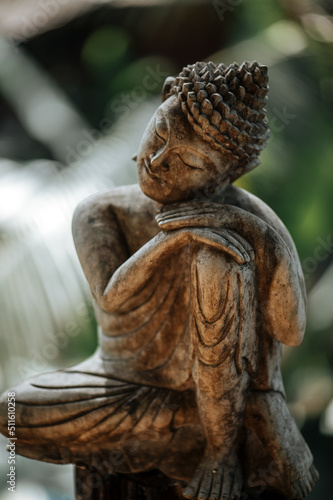 Statuette of Buddha on a background of green leaves close up